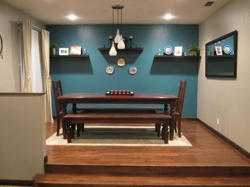 A dining room with a teal feature wall, a long wooden table and a bench